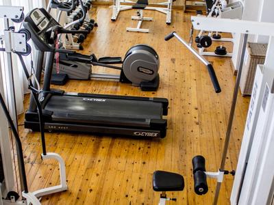 Ein heller Fitnessraum mit Holzfußboden und verschiedenen Trainingsgeräten, darunter Laufbänder und Gewichte.