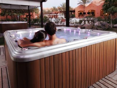 Zwei Personen entspannen in einem modernen, rechteckigen Whirlpool mit Holzverkleidung im Außenbereich.