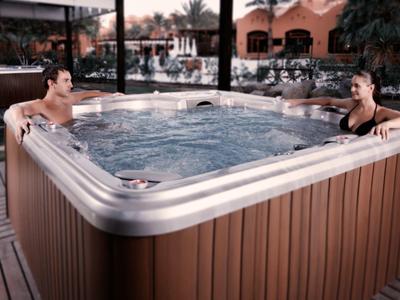 Zwei Personen sitzen entspannt in einem großen, beleuchteten Whirlpool im Freien bei Dämmerung.