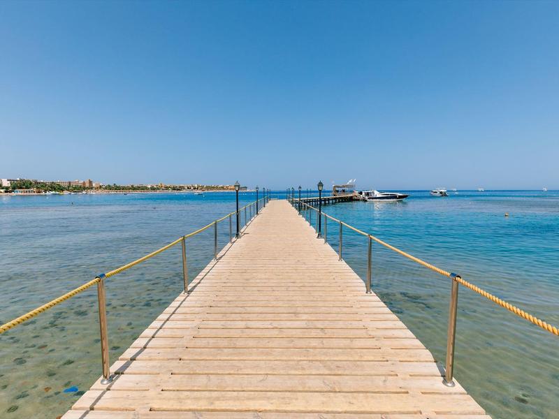 A long wooden pier stretches over clear blue water under a cloudless sky.