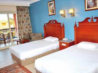 Chambre d'hôtel avec deux lits simples, mur accent bleu, table de nuit et balcon