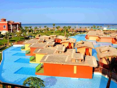 Vista di un resort con piscine, bungalow e il mare sullo sfondo.