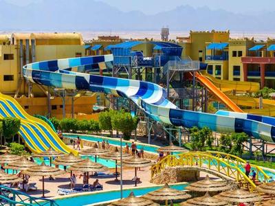 Großer Wasserpark mit bunten Rutschen vor modernen Hotelgebäuden unter blauem Himmel.