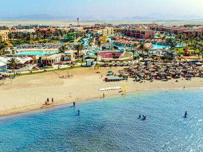 Strand mit Liegestühlen und Sonnenschirmen vor einem großen Resort an der Küste.