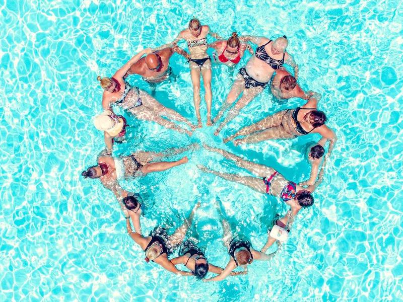 Groupe de personnes nageant en forme de cœur dans une piscine, vu d'en haut.