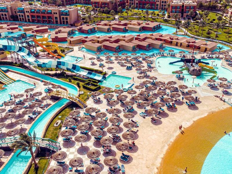Grand complexe aquatique avec piscines, toboggans et parasols sur une plage de sable.