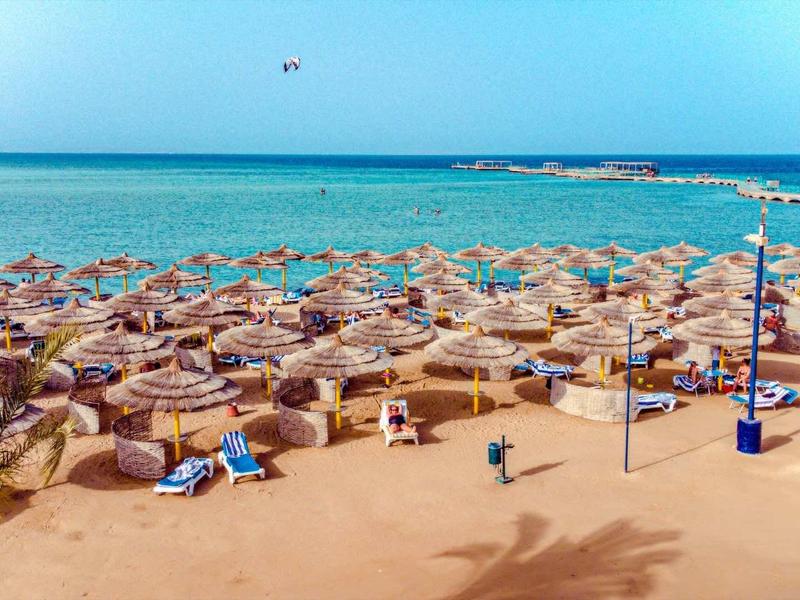 Plage avec de nombreux parasols et transats au bord de la mer turquoise calme.