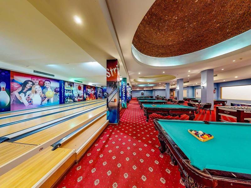 Intérieur d'un centre de loisirs avec pistes de bowling et table de billard sur moquette rouge.