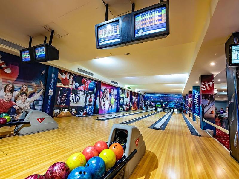 Vue intérieure d'une piste de bowling avec des boules colorées et un tableau de scores numérique.