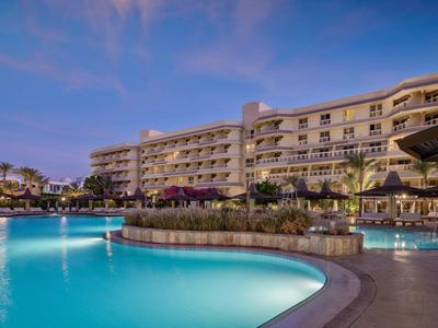 Groot hotel met verlicht zwembad bij schemering onder een bewolkte lucht.