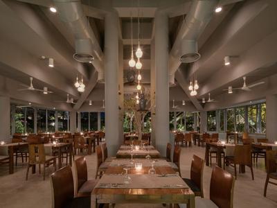 Restaurant met warme verlichting, houten tafels en stoelen, grote ramen en decoratieve lampen.