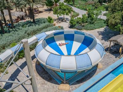 Bovenaanzicht van een ronde glijbaan in een waterpark omgeven door planten en paden.