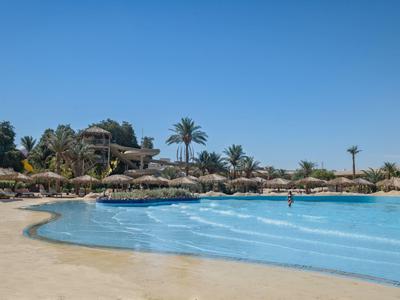 Grande piscina con ombrelloni e palme sotto un cielo azzurro limpido in un resort.