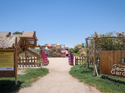 Pad naar Secret Garden met houten poorten, planten en kleurrijke zitplaatsen onder blauwe lucht.