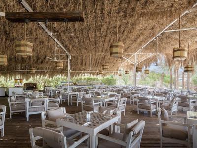 Open restaurant met witte houten tafels en een rieten dak in een tropische omgeving