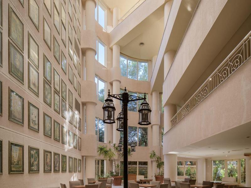 Área luminosa del vestíbulo del hotel con asientos, paredes altas y dos faroles en el patio interior.
