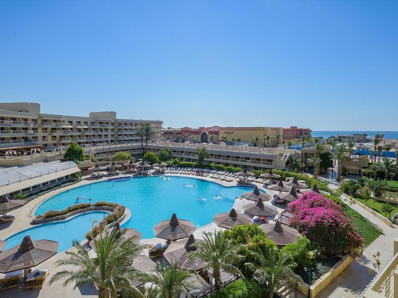 Amplia piscina en forma de riñón en un hotel junto al mar con tumbonas y vegetación exuberante.