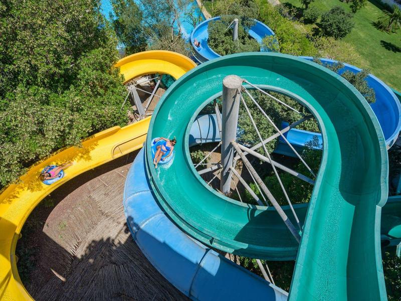 Toboganes de agua de colores en un parque acuático rodeado de árboles y césped.