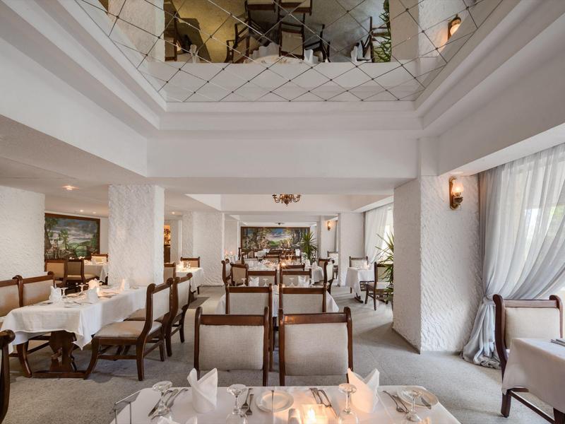 Restaurante iluminado con paredes blancas, mesas preparadas y sillas de madera marrón en un hotel.