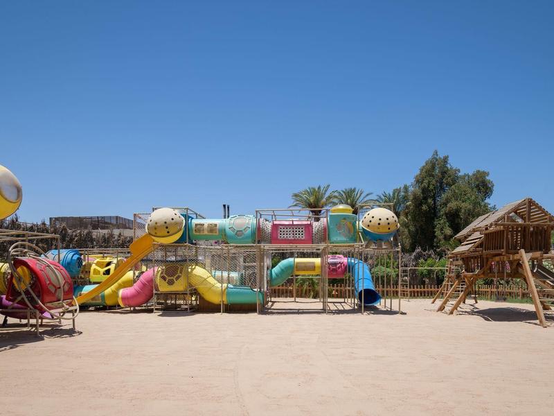 Parque infantil colorido en área al aire libre con suelo arenoso bajo un cielo despejado.