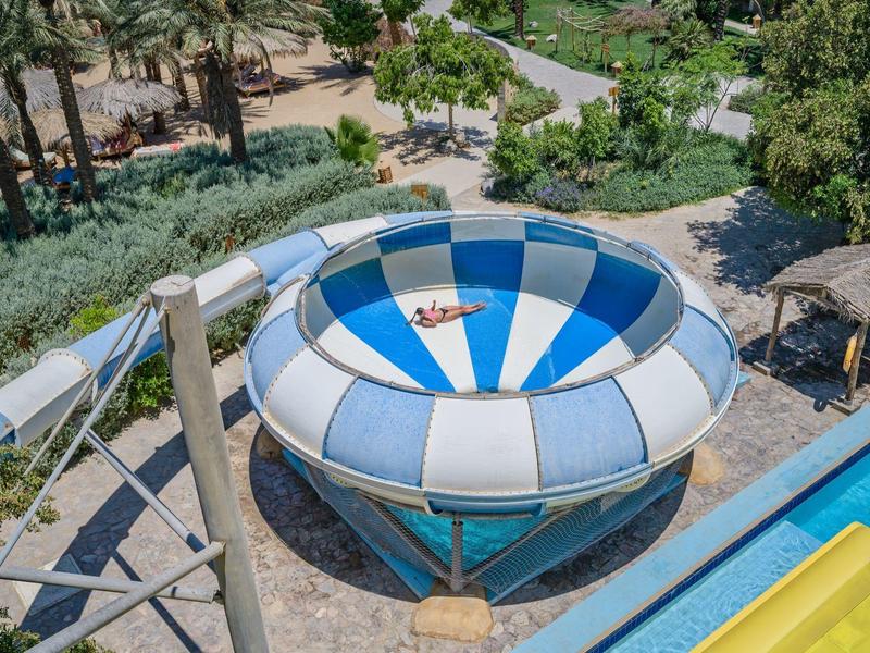 Tobogán de agua colorido en un parque acuático al aire libre con palmeras y caminos