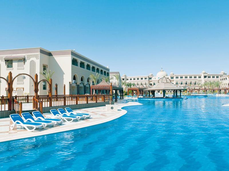 Velký venkovní bazén s lehátky před hotelem pod jasnou oblohou.