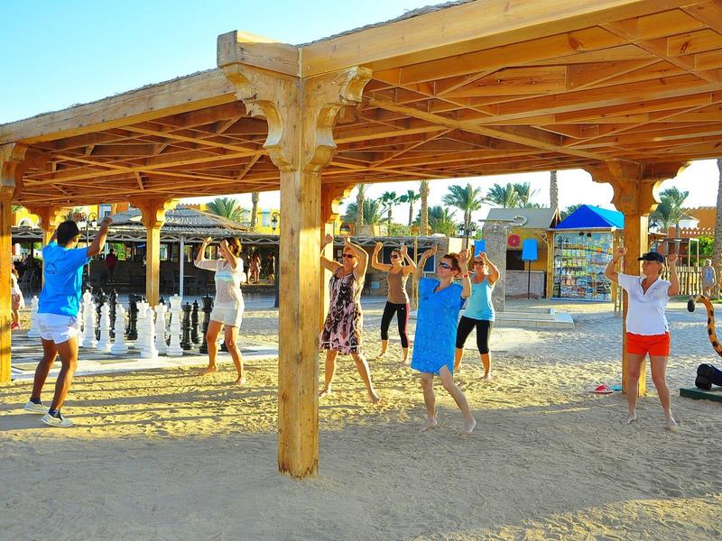 Děti si hrají pod dřevěnou konstrukcí na písku za slunečného dne.