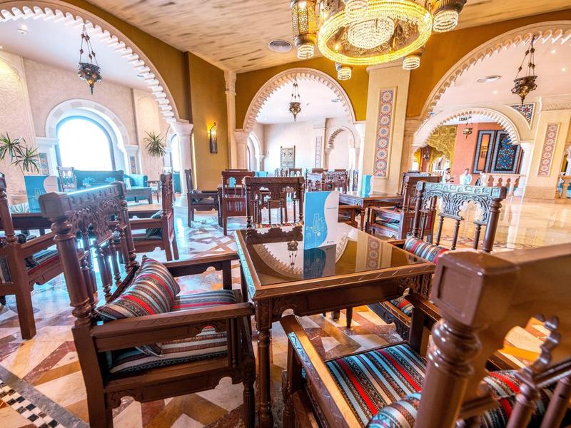 Světla hotelová jídelna s dřevěným nábytkem a barevnými polštáři pod klenutými stropy.