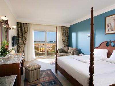 Helles Schlafzimmer mit vierpfostenbett, blauem Akzentwand, Sofa und Balkon mit Meeresblick.