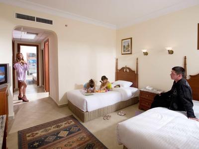 Hotelzimmer mit zwei Einzelbetten, Teppich, Fernseher und drei Personen, eine am Bett, zwei am Eingang.