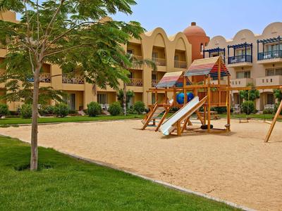 Innengarten mit Spielplatz, Sandfläche, Rutsche, Klettergerüst und zweistöckigem Gebäude im Hintergrund.