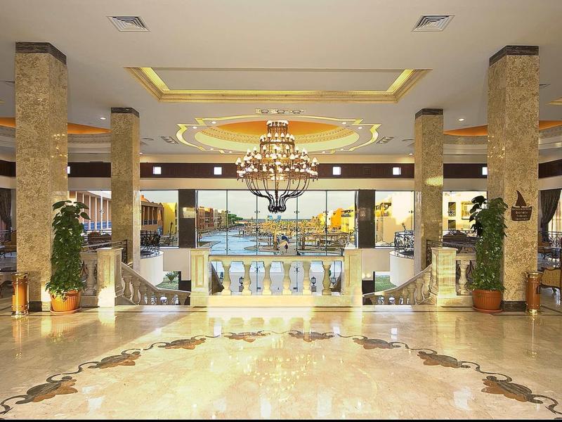 Prostorná hotelová lobby s mramorovou podlahou, lustry a dekorativními sloupy.