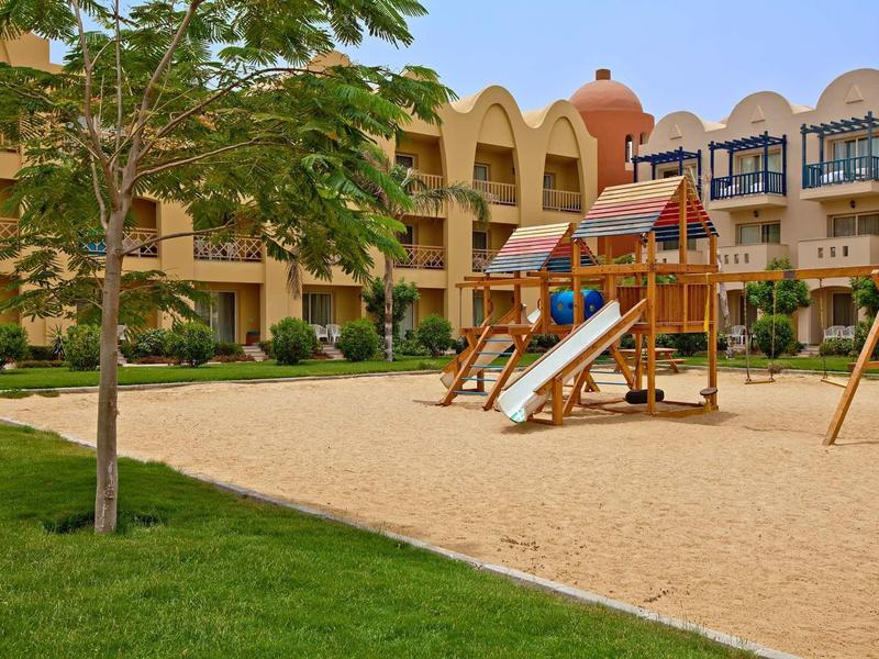 Dětské hřiště se skluzavkou a houpačkou před dvoupodlažním hotelem s balkony