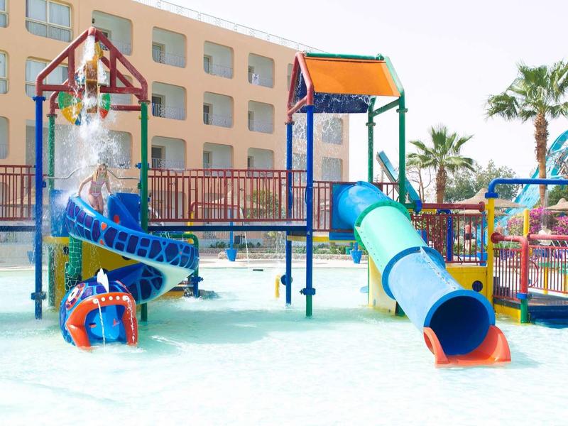Barevné dětské hřiště s skluzavkami a vodními prvky v hotelovém areálu.