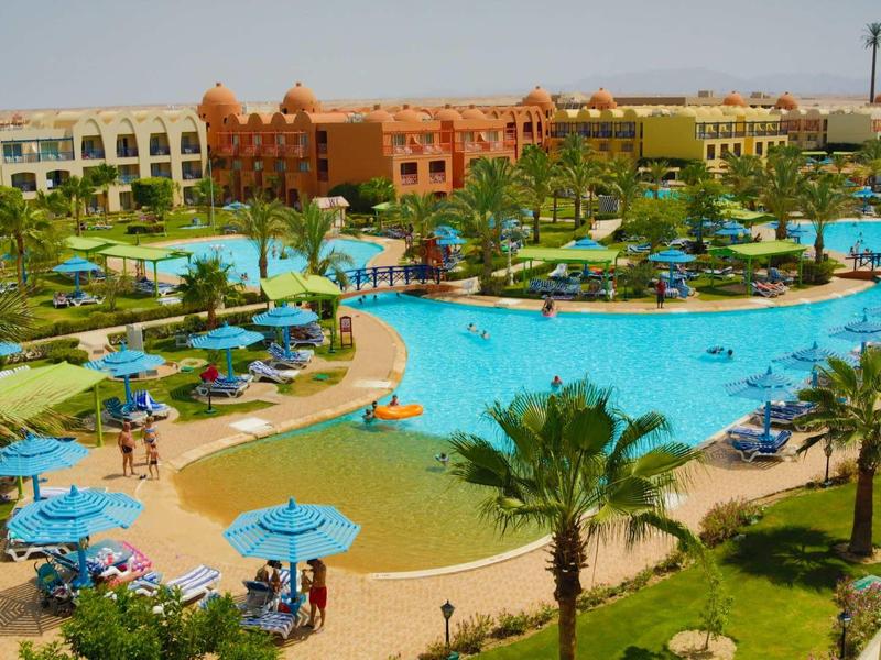 Hotelový areál s několika bazény, tyrkysovou vodou, lehátky a slunečníky v tropickém prostředí.