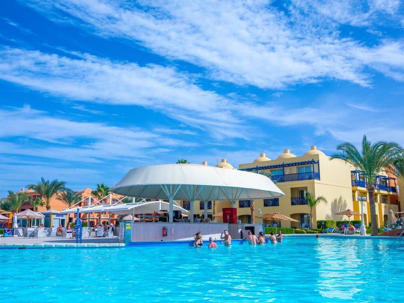 Bar u bazénu v hotelovém resortu pod modrou oblohou s palmami a hosty v bazénu.