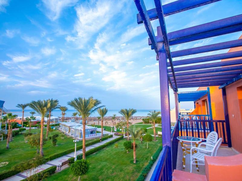 Balkon s židlemi s výhledem na tropickou zahradu a moře pod modrou oblohou.