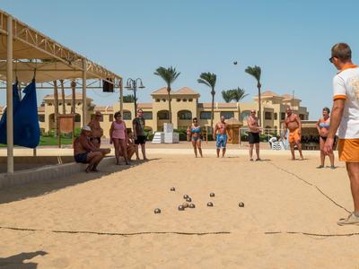 Personas juegan a la petanca en una cancha de arena cerca de edificios del hotel y palmeras.