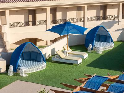 Terraza del hotel con tumbonas y sombrillas azules sobre césped verde.