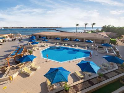 Gran piscina del hotel con sombrillas azules, tumbonas y vistas al mar bajo un cielo despejado.