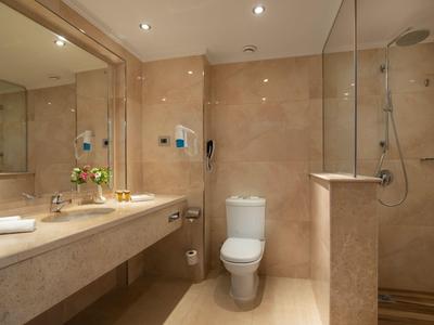 Moderní hotelová koupelna s velkým zrcadlem, umyvadlem, toaletou a sprchou s skleněnou příčkou.