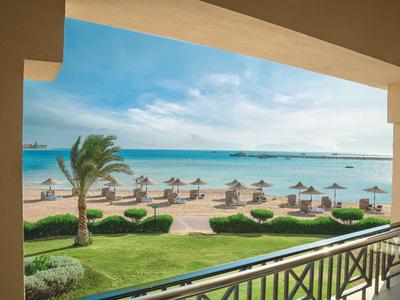Vista desde un balcón hacia una playa con sombrillas y palmeras junto al mar.