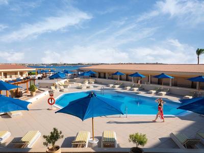 Gran área de piscina de hotel con sombrillas azules y tumbonas bajo un cielo azul.