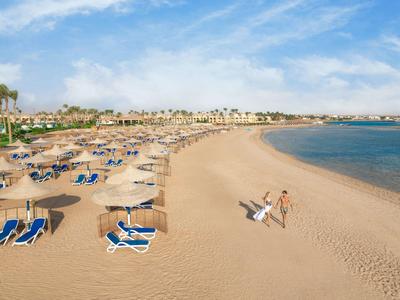 Slunečná písečná pláž s lehátky, slunečníky a několika lidmi u klidného moře.