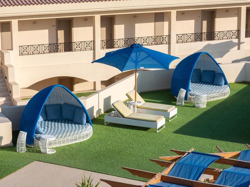 Pohodlné lounge oblasti s modrými slunečníky a lehátky na zelené trávě v hotelu