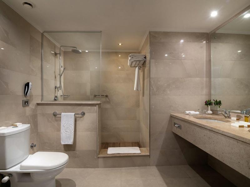 Moderní hotelová koupelna se sprchovým koutem, velkým zrcadlem a mramorovým umyvadlem.