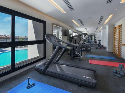 Moderner Fitnessraum mit Laufbändern, Trainingsmatten und großem Fenster zum Außenpool.