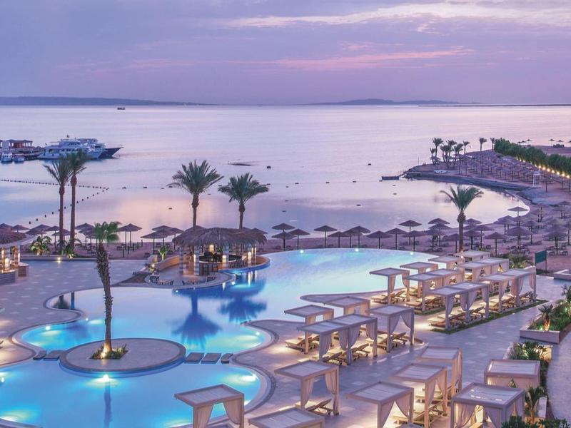 Luxurious resort with poolside loungers, palm trees, and ocean view at sunset.