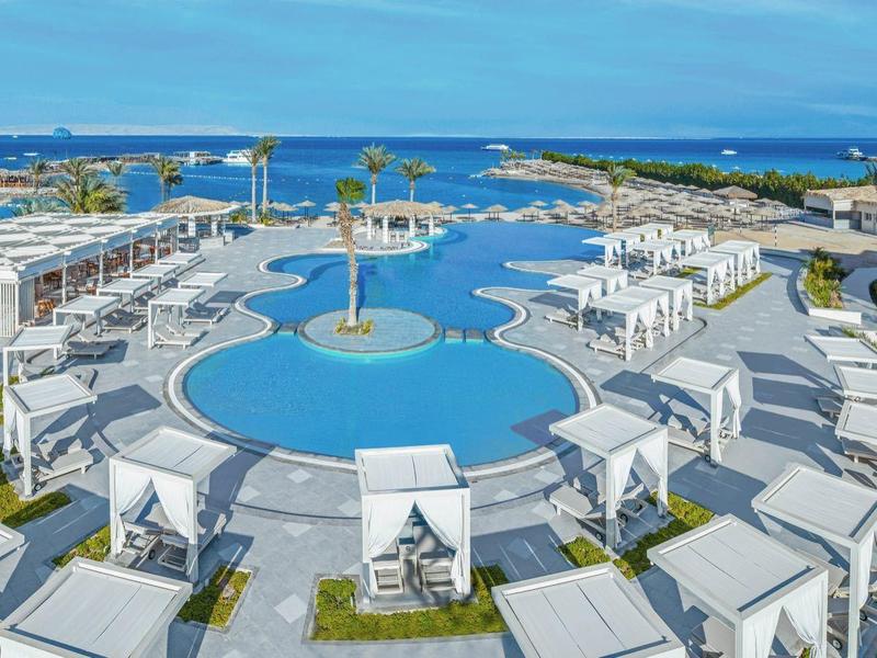 Luxury resort with circular pool, white cabanas, and ocean view under blue sky.