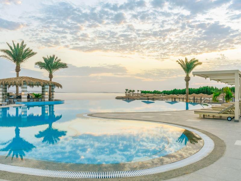 Luxurious poolside area with palm trees, sunbeds, and a calm sky reflecting on the water.